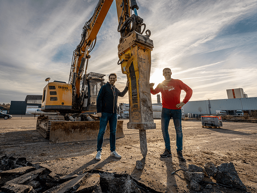 Spatenstich - Marc und Jochen Böck vor einem Abrissbagger auf dem zukünftigen Firmengelände